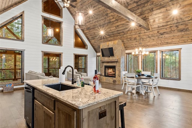 kitchen with sink, hanging light fixtures, high vaulted ceiling, wooden walls, and a center island with sink