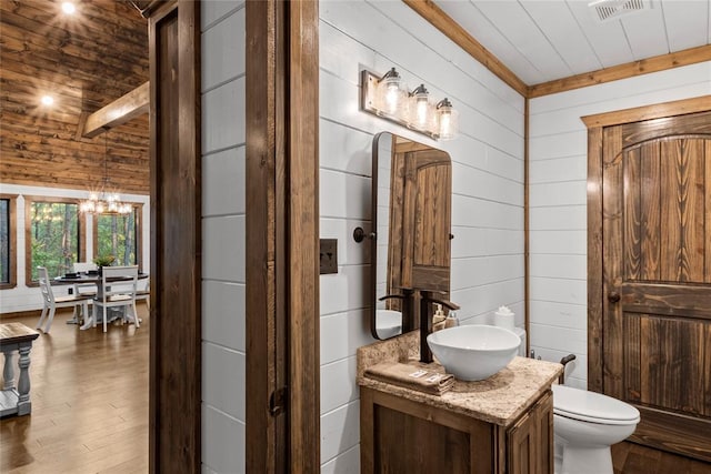 bathroom with wood walls, hardwood / wood-style floors, a chandelier, toilet, and vanity