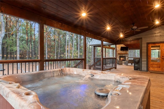 interior space with an outdoor stone fireplace, a hot tub, and ceiling fan