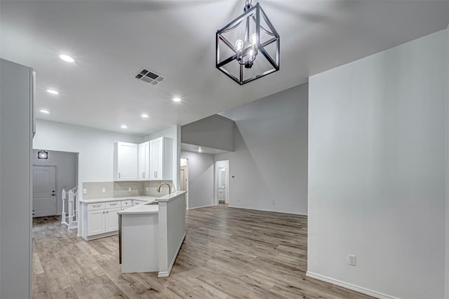 kitchen featuring sink, backsplash, kitchen peninsula, white cabinets, and light wood-type flooring