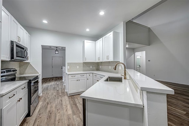 kitchen with backsplash, sink, light hardwood / wood-style flooring, appliances with stainless steel finishes, and white cabinetry