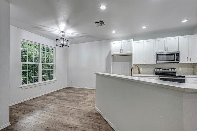 kitchen with pendant lighting, light hardwood / wood-style floors, white cabinetry, and appliances with stainless steel finishes