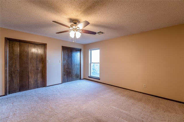 unfurnished bedroom featuring ceiling fan, light colored carpet, a textured ceiling, and two closets