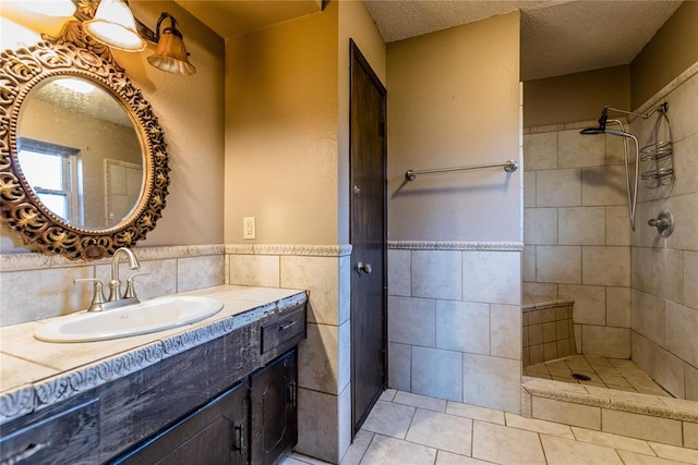 bathroom featuring tile patterned floors, vanity, a textured ceiling, tiled shower, and tile walls