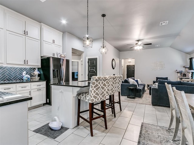 kitchen featuring stainless steel refrigerator with ice dispenser, a kitchen island with sink, ceiling fan, pendant lighting, and white cabinetry