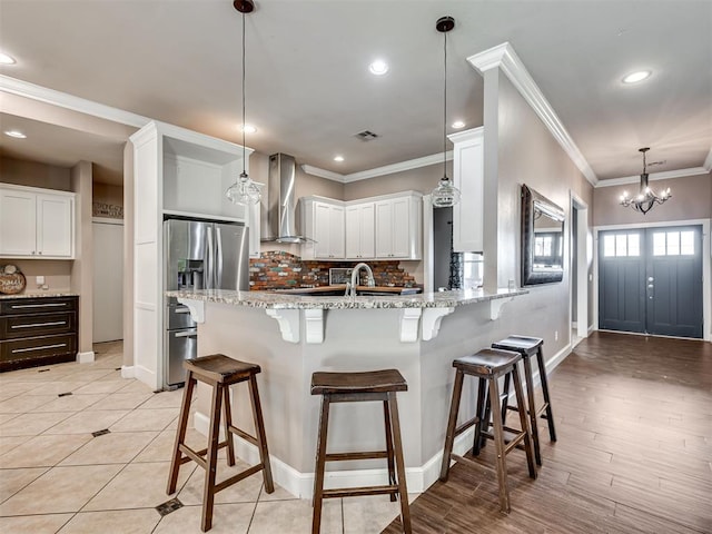 kitchen featuring white cabinets, a kitchen bar, wall chimney range hood, and hanging light fixtures