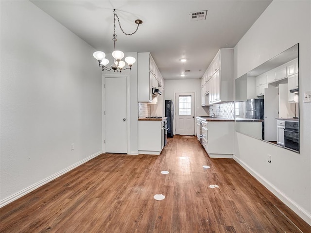 kitchen with decorative backsplash, hardwood / wood-style floors, white cabinetry, and a notable chandelier