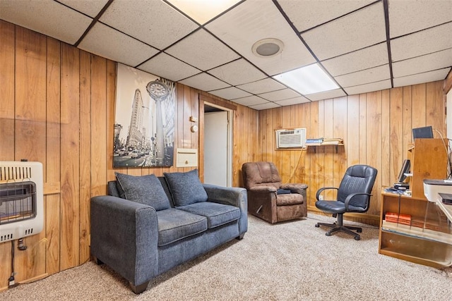 living room with heating unit, a wall mounted air conditioner, a drop ceiling, light colored carpet, and wood walls