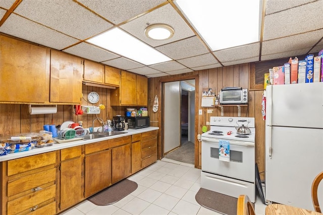 kitchen featuring sink, a paneled ceiling, white appliances, and wood walls