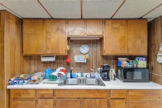 kitchen featuring sink, a paneled ceiling, and wood walls