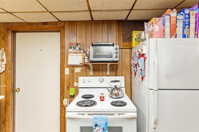 kitchen with a drop ceiling, white appliances, and wood walls