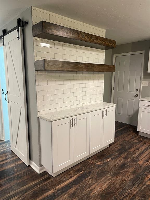 kitchen featuring light stone countertops, tasteful backsplash, a barn door, dark hardwood / wood-style flooring, and white cabinets