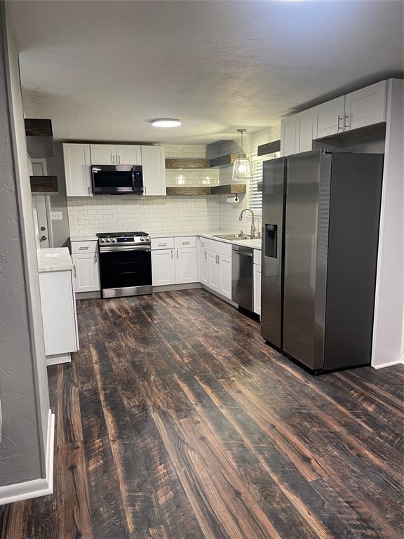 kitchen with decorative backsplash, appliances with stainless steel finishes, dark hardwood / wood-style flooring, decorative light fixtures, and white cabinets