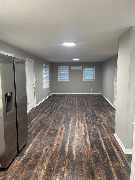 basement with a wall mounted AC, stainless steel fridge with ice dispenser, and dark hardwood / wood-style flooring