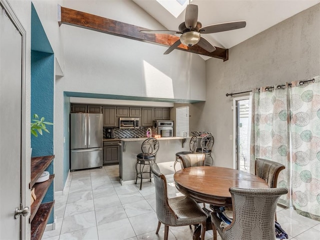 dining room with beam ceiling, a skylight, ceiling fan, and high vaulted ceiling