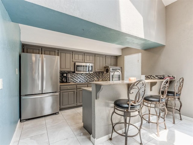 kitchen featuring a kitchen breakfast bar, gray cabinets, appliances with stainless steel finishes, and tasteful backsplash