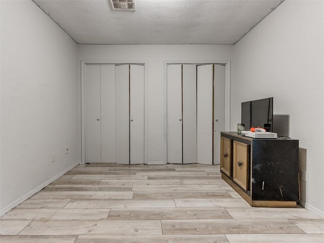 unfurnished bedroom with multiple closets, a textured ceiling, and light hardwood / wood-style flooring