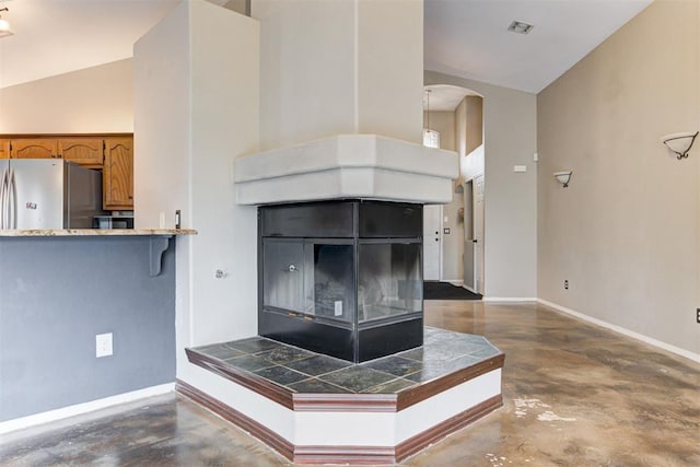 kitchen with a tiled fireplace, high vaulted ceiling, stainless steel refrigerator, and kitchen peninsula