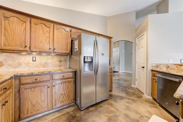 kitchen with light stone counters, appliances with stainless steel finishes, concrete flooring, and decorative backsplash