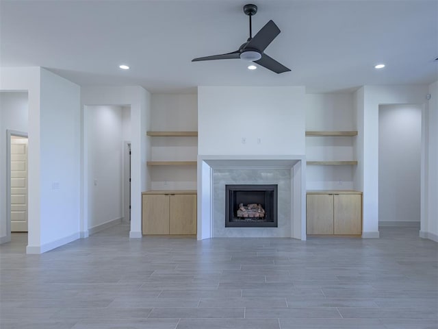 unfurnished living room featuring built in shelves, ceiling fan, light wood-type flooring, and a fireplace