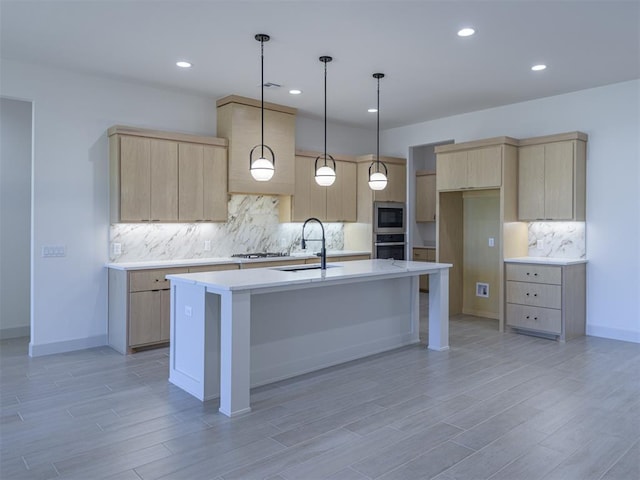 kitchen featuring light brown cabinets, sink, stainless steel appliances, decorative light fixtures, and a center island with sink