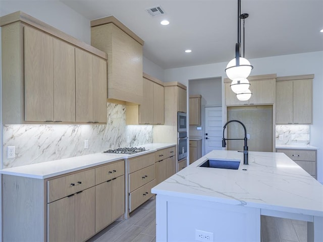 kitchen featuring a kitchen island with sink, sink, decorative light fixtures, and light brown cabinets