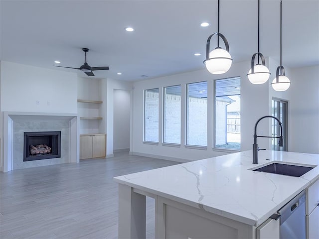 kitchen with sink, light stone counters, light hardwood / wood-style flooring, an island with sink, and pendant lighting