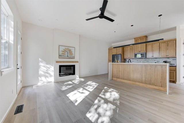 kitchen with tasteful backsplash, light hardwood / wood-style flooring, decorative light fixtures, black refrigerator, and a kitchen island