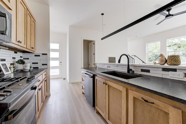 kitchen featuring decorative backsplash, appliances with stainless steel finishes, sink, pendant lighting, and light hardwood / wood-style flooring