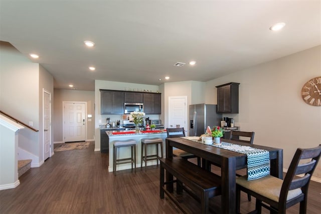 kitchen with a kitchen breakfast bar, dark brown cabinetry, stainless steel appliances, a kitchen island with sink, and dark hardwood / wood-style floors