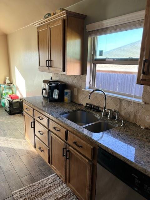 kitchen featuring stainless steel dishwasher, decorative backsplash, dark stone countertops, and sink