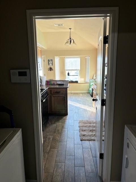 kitchen with black range, an inviting chandelier, washing machine and clothes dryer, and light hardwood / wood-style flooring