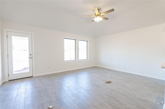 empty room with baseboards, a ceiling fan, light wood-style floors, and vaulted ceiling