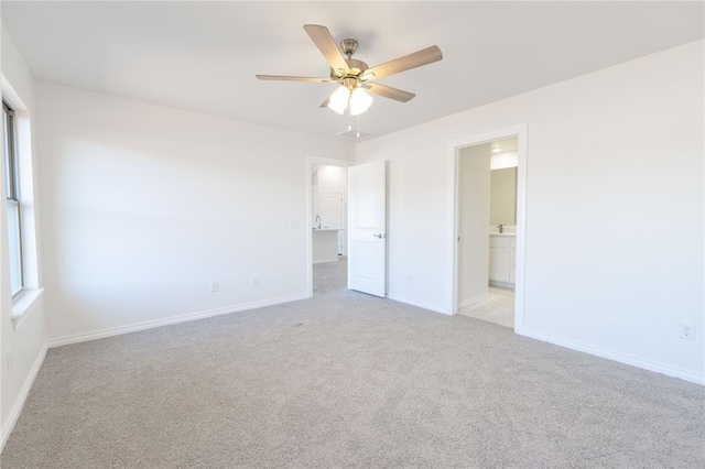 unfurnished bedroom featuring light colored carpet, ensuite bathroom, baseboards, and multiple windows