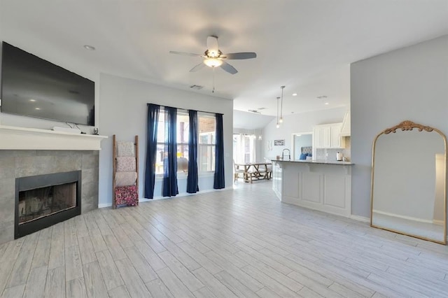 unfurnished living room with ceiling fan, a fireplace, light hardwood / wood-style floors, and sink