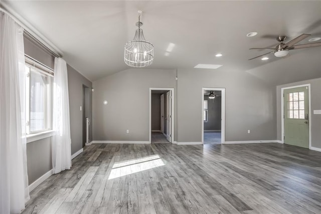 spare room featuring ceiling fan with notable chandelier, wood-type flooring, and lofted ceiling