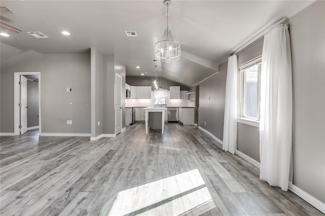 kitchen with a center island, hanging light fixtures, vaulted ceiling, white cabinets, and appliances with stainless steel finishes