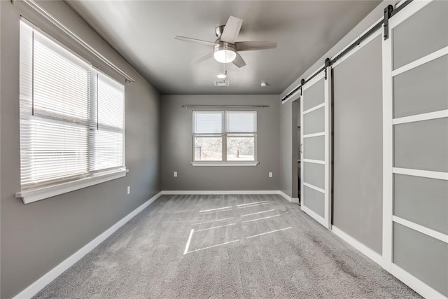 unfurnished bedroom with a barn door, ceiling fan, and carpet