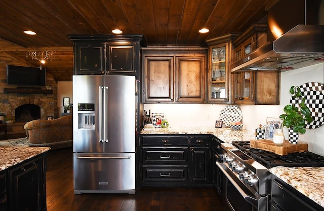 kitchen featuring light stone countertops, wall chimney exhaust hood, premium appliances, dark hardwood / wood-style floors, and a fireplace