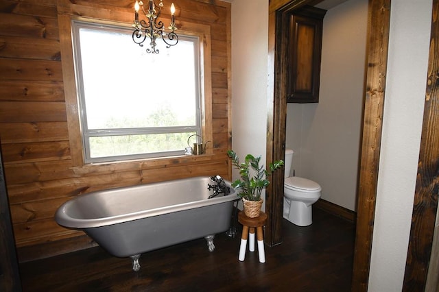 bathroom with hardwood / wood-style floors, an inviting chandelier, wooden walls, toilet, and a tub to relax in