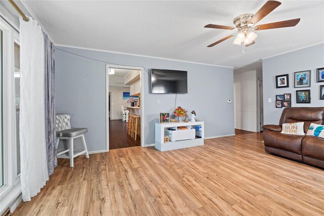 living room featuring a textured ceiling, light wood-type flooring, ceiling fan, and crown molding