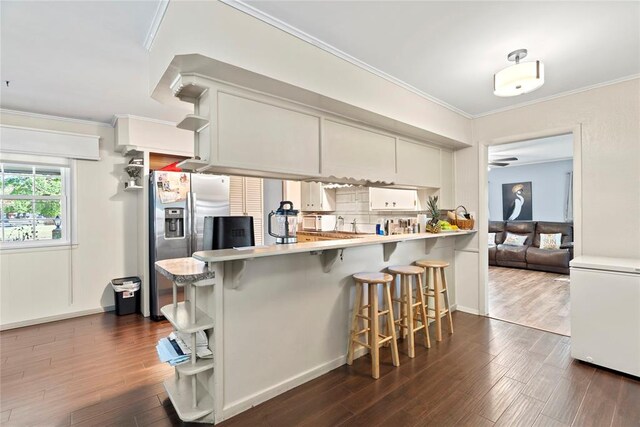 kitchen featuring kitchen peninsula, a kitchen breakfast bar, stainless steel refrigerator with ice dispenser, dark wood-type flooring, and white cabinets