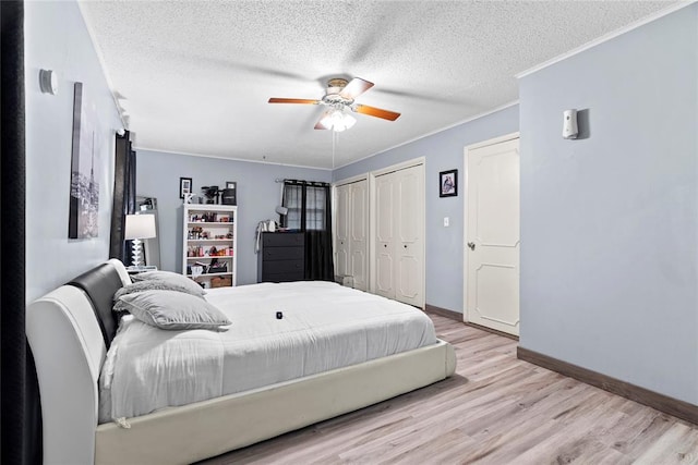 bedroom with ceiling fan, light hardwood / wood-style floors, a textured ceiling, two closets, and ornamental molding