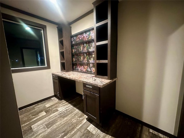 bar featuring wood-type flooring, built in desk, light stone counters, and dark brown cabinets