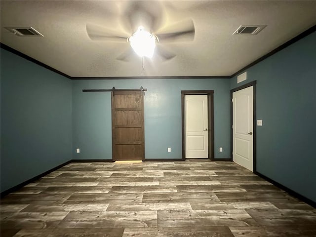 unfurnished bedroom with ceiling fan, a barn door, wood-type flooring, and crown molding