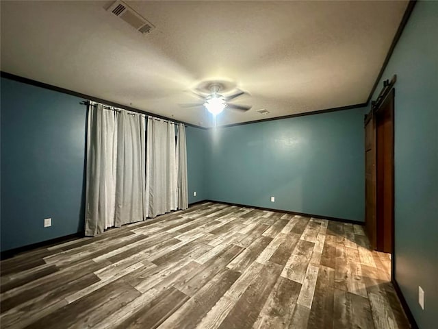 unfurnished room featuring a textured ceiling, ceiling fan, crown molding, a barn door, and hardwood / wood-style flooring