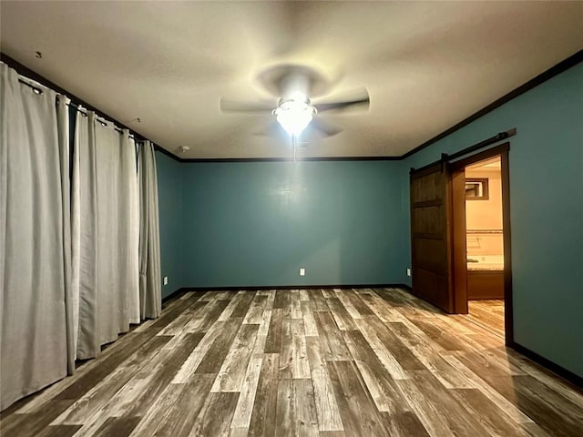 unfurnished bedroom with hardwood / wood-style floors, ceiling fan, a barn door, ornamental molding, and connected bathroom