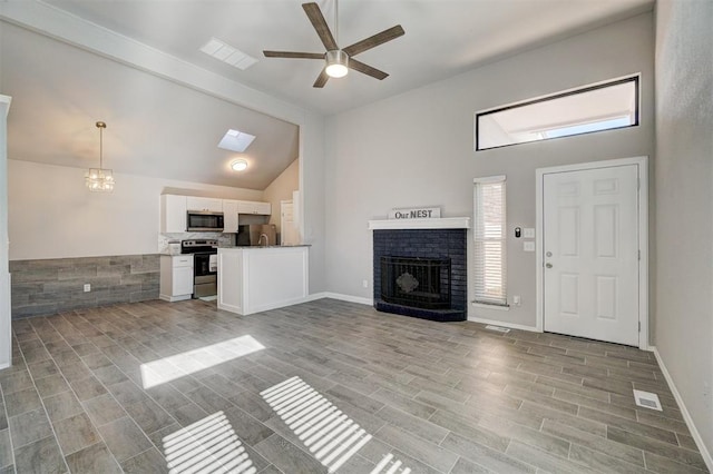 unfurnished living room with ceiling fan, high vaulted ceiling, light hardwood / wood-style floors, and a brick fireplace