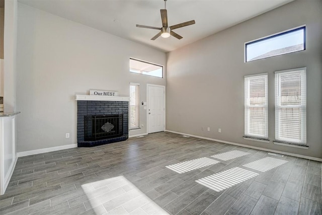 unfurnished living room with ceiling fan, light hardwood / wood-style floors, a fireplace, and a high ceiling