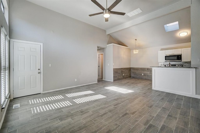 unfurnished living room with high vaulted ceiling, ceiling fan with notable chandelier, a skylight, light wood-type flooring, and beam ceiling